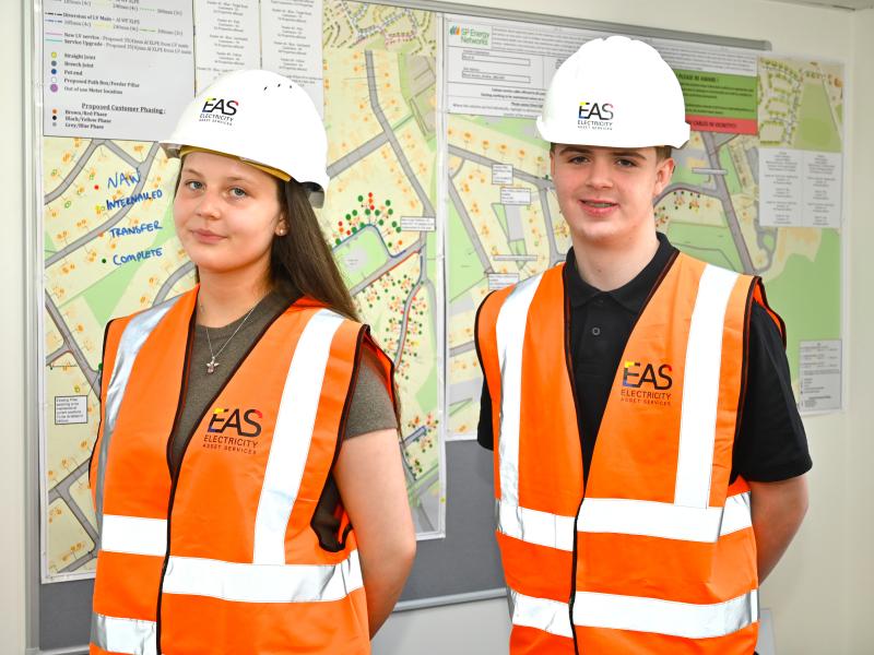 Summer Placement participants wearing hard hats and high-visibility safety vests stand in front of maps and planning displays in an office environment.