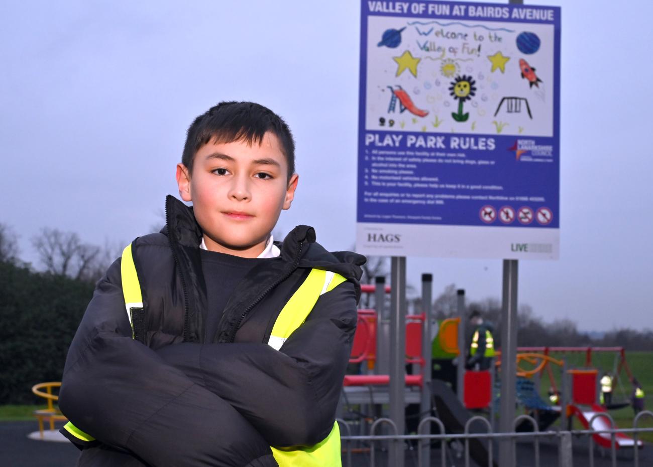 young child stands in front of play park sign