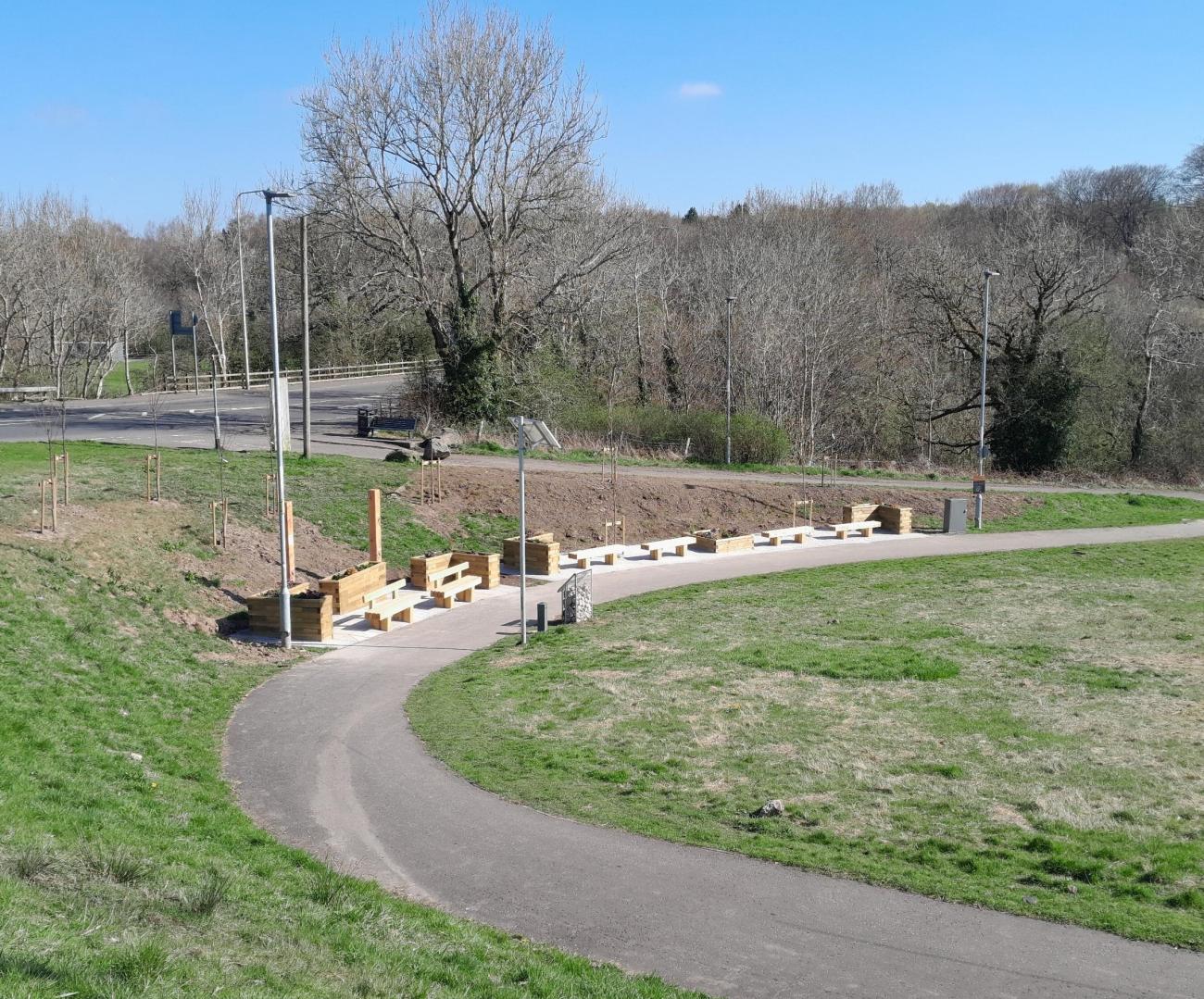 Walk way with new benches and planters next to grassy ground. 
