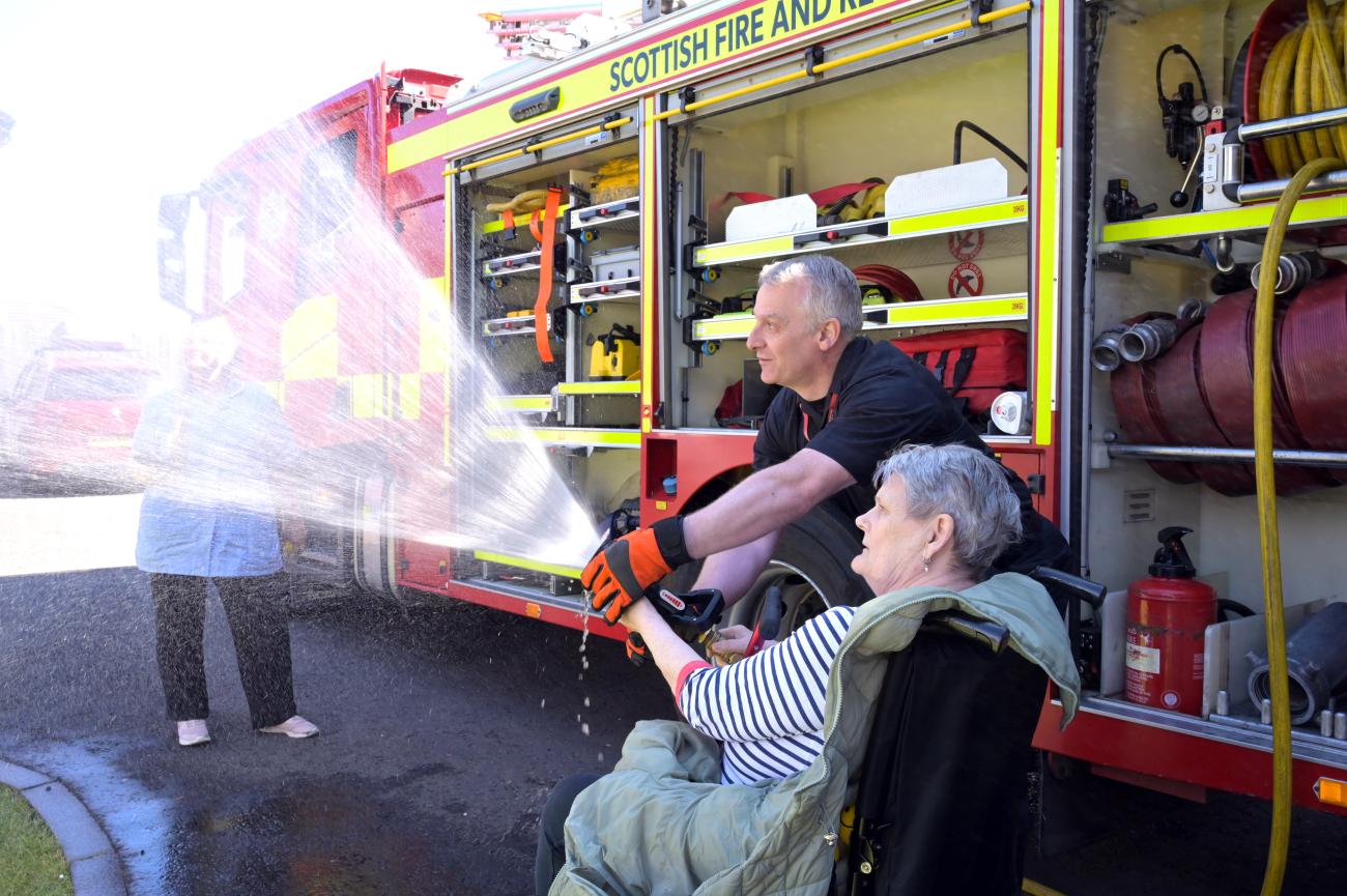 Member of the community and fire fighter spraying a fire hose from the fire truck