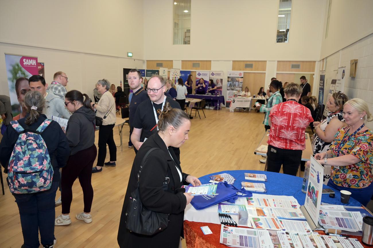 a wide photograph displaying various people within a hall interacting with information stalls