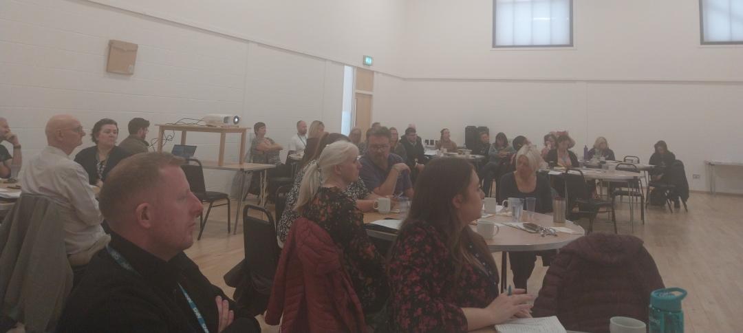 Community and voluntary leads in a presentation hall seated around multiple tables