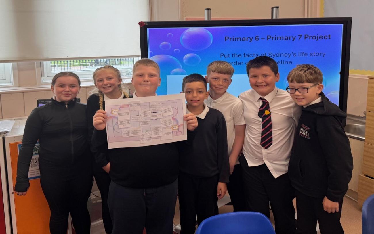 Pupils gathered around for a photograph holding up an image for camera