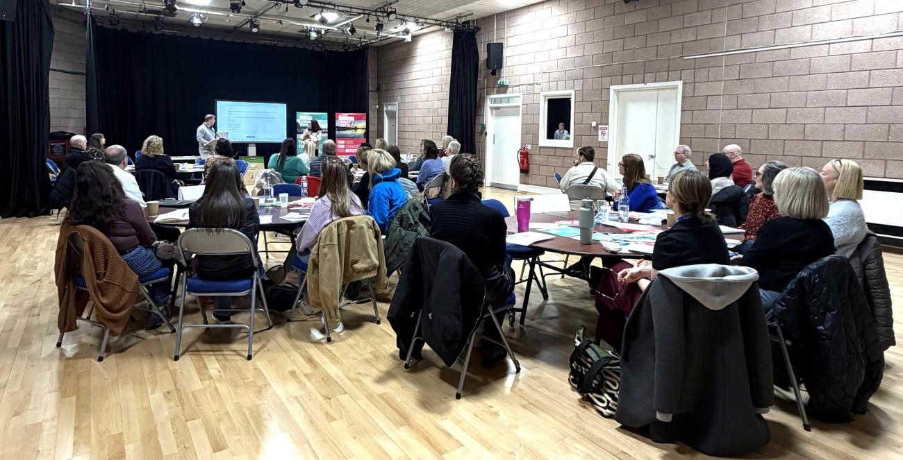 Community Partners in a large room sitting watching a presentation on the community priorities 
