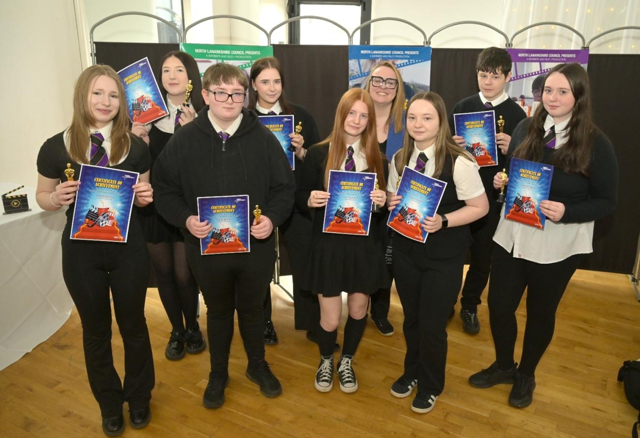 Students posing for a photo holding up posters and awards