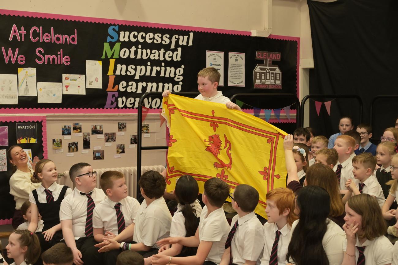 Young pupil standing with Lion Rampant flag in assembly hall among other pupils