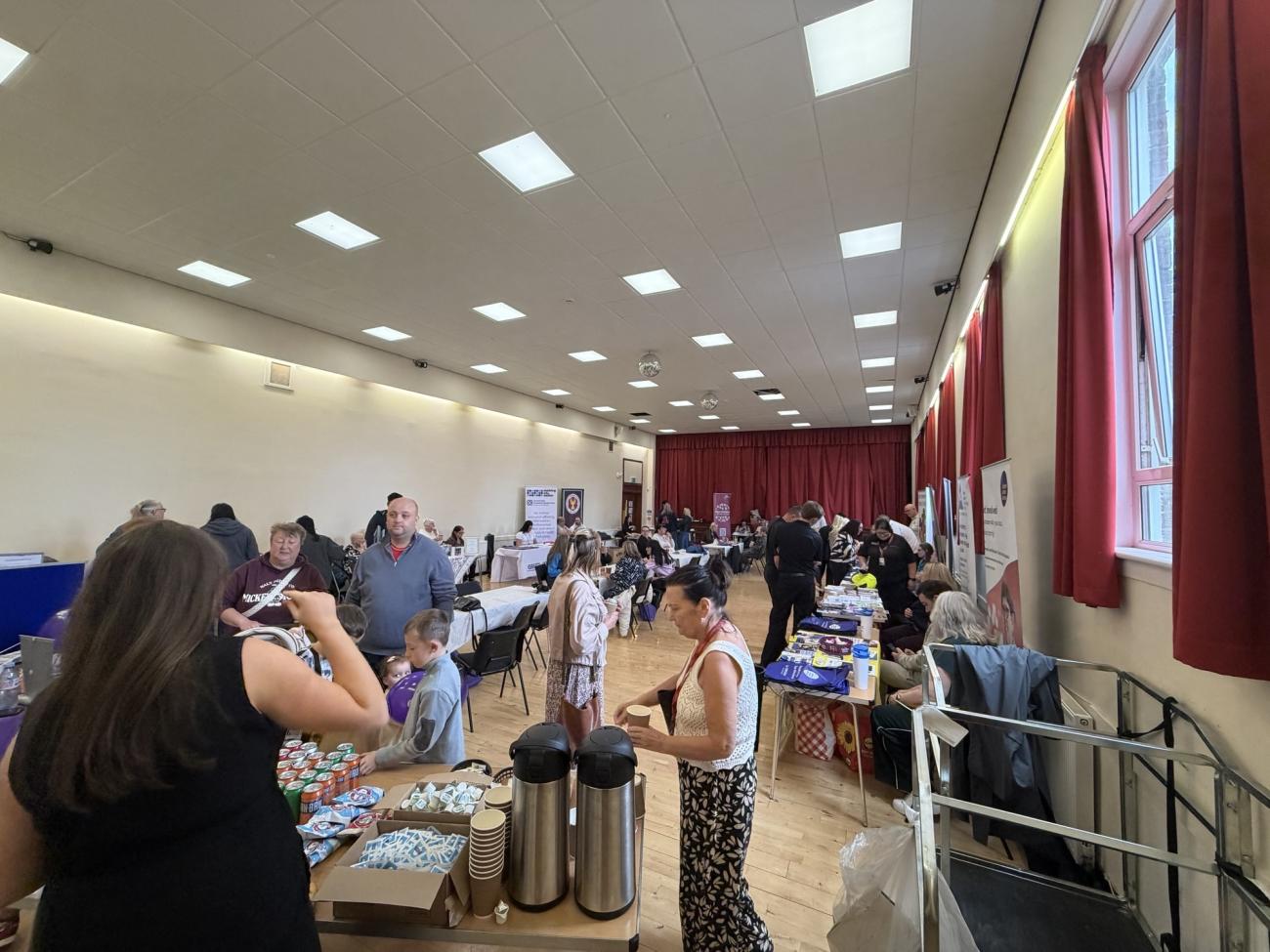People standing in hall looking at stalls and having tea