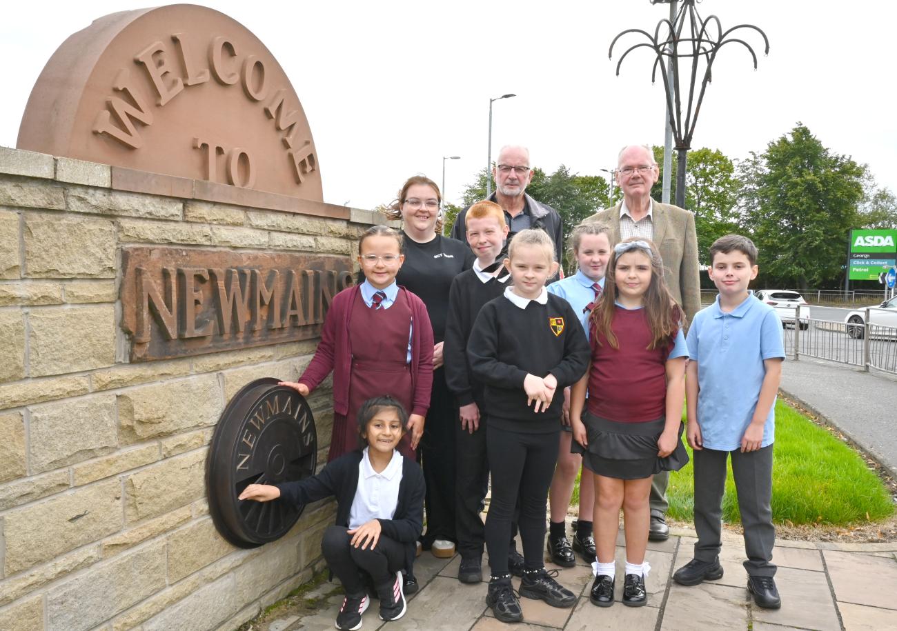 Pupils posing beside the welcome to Newmains wall and sign. 