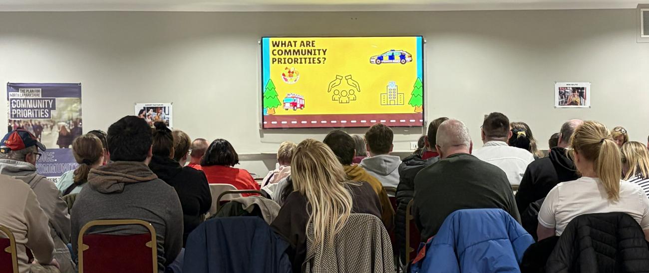 people sitting in a room in rows of chairs looking at presentation screen on wall