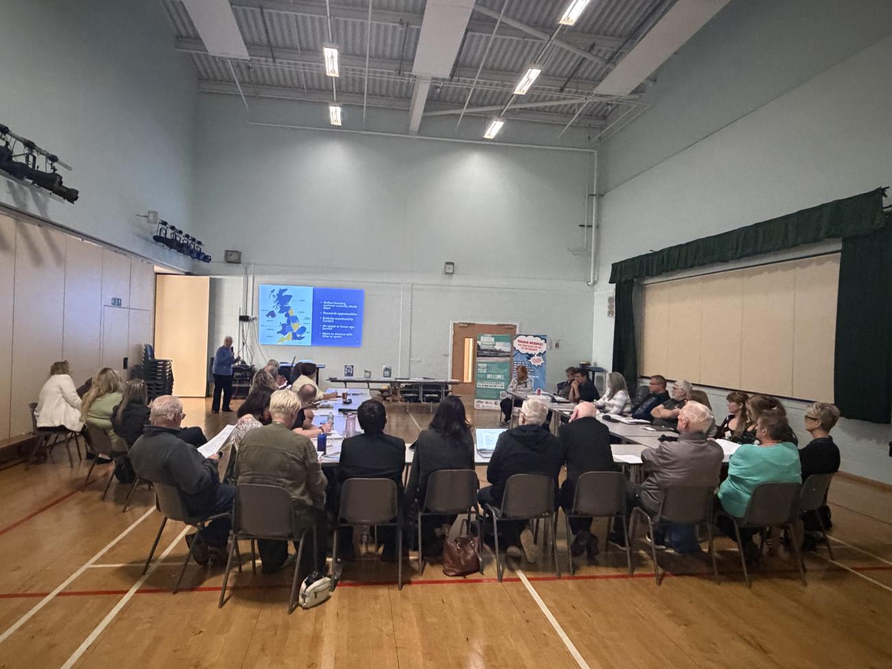 people sitting round tables listening to man talking at projector screen